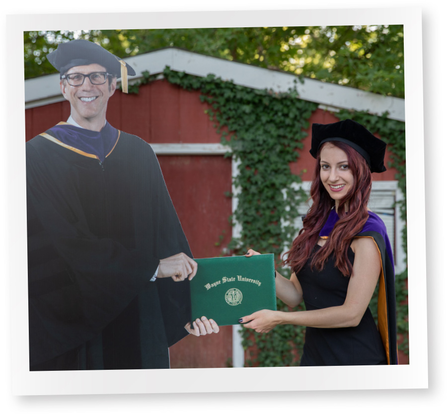 polaroid of female student holding degree with cardboard cut out of dean