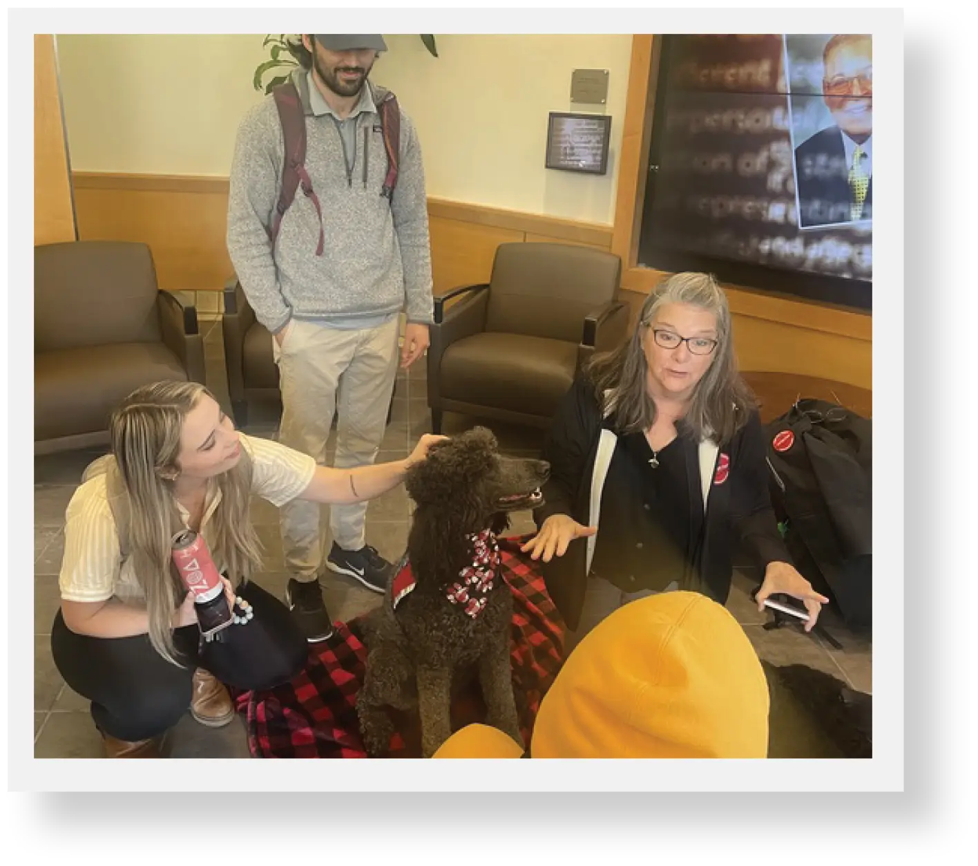 Two students petting black poodle therapy dog and instructor in mid explaination