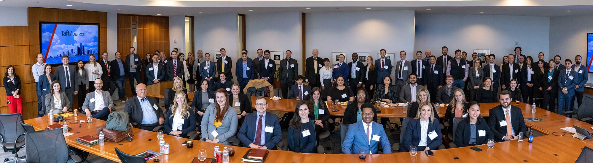 Numerous students and judges at the Wayne State Jaffe/Taft Transactional Law Invitational smile and pose for a picture as many stand and others are seated at a large conference table in their business attire.