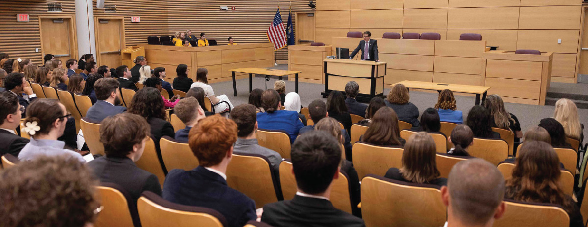 dean speaking at podium to full auditorium