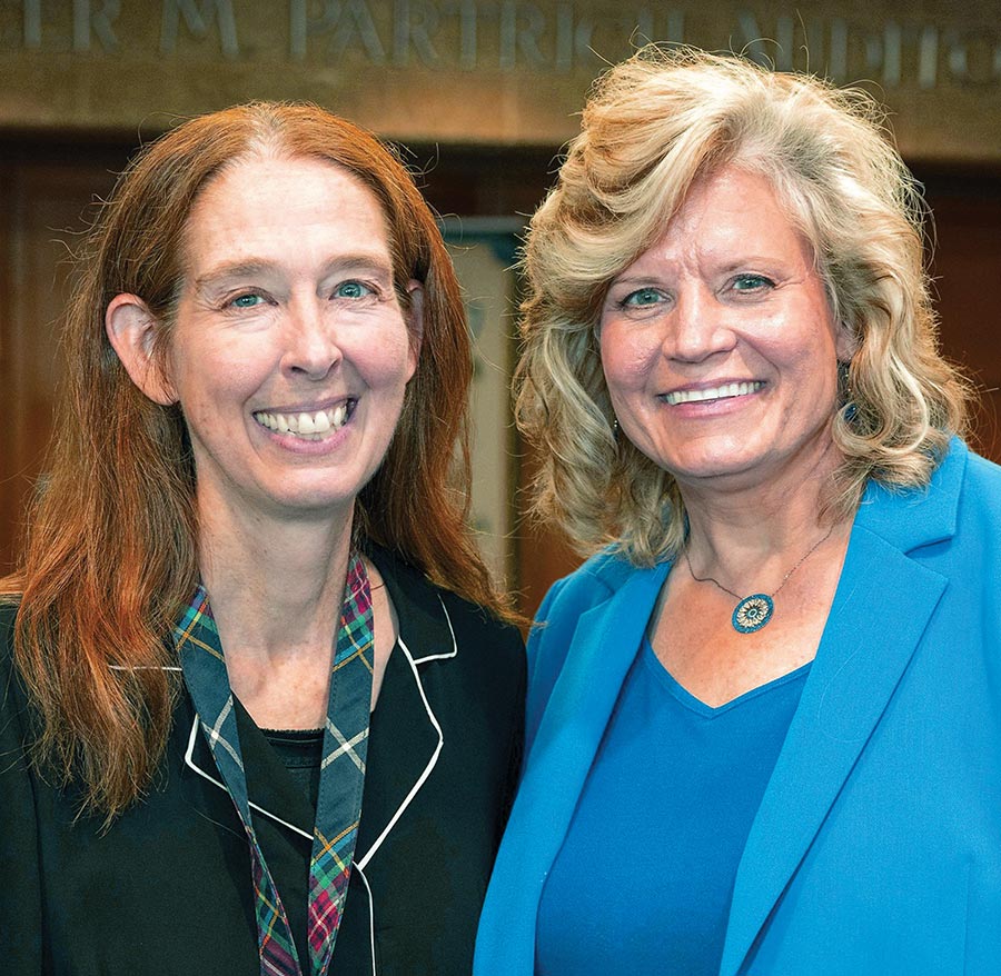 Two women in professional attire smiling together for a close-up portrait.